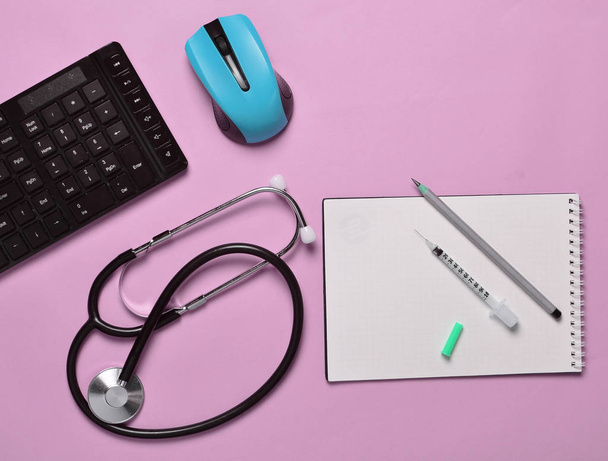 Nykyaikaisen lääkärin työpaikka. Näppäimistö, langaton hiiri, muistikirja, stetoskooppi, ruisku sinisellä pastellitaustalla, ylhäältä katsottuna, minimalistinen tren
 - Valokuva, kuva