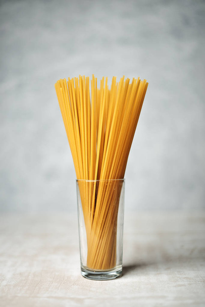 bunch of raw spaghetti in glass on wooden table  - Foto, imagen