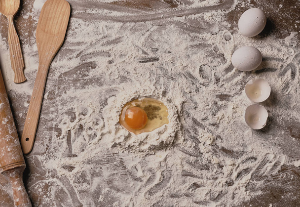 top view of wooden table covered by flour and egg yolk for dough preparation  - Photo, image