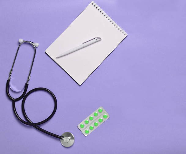 Cuaderno, tabletas y estetoscopio médico sobre un fondo pastel azul, tendencia minimalista, vista superior, placa de trabajo médica
 - Foto, imagen