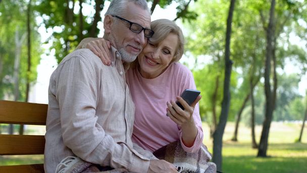 Smiling retired woman holding smartphone and hugging handsome husband, app - Photo, Image