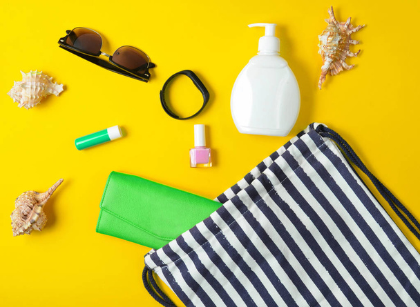 Strandtasche und Accessoires zum Entspannen am Strand auf gelbem Pastell-Hintergrund. das Konzept des Seebades, Sommerzeit. Draufsicht, flach, minimalistisch - Foto, Bild