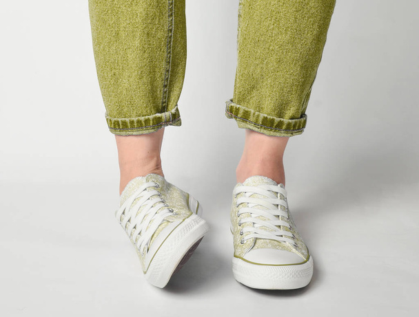Vrouwelijke benen Kortom jeans en sneakers staan op een witte pagina - Foto, afbeelding