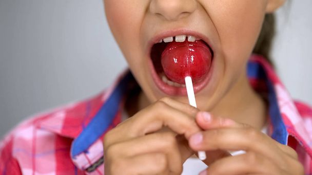 Cute little girl trying to bite lollipop, effect of sugar on teeth, dental care - Foto, Imagem