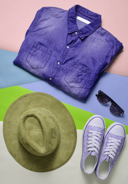 Vrouwen mode kleding en accessoires. Denim overhemd, sneakers, vilten hoed, zonnebril, lay-out op een gekleurde achtergrond. Bovenaanzicht, platte la - Foto, afbeelding