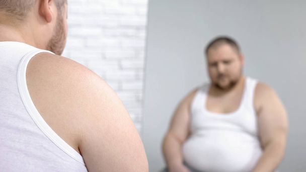 Uomo obeso guardando il suo specchio riflesso, problema di sovrappeso e insicurezze
 - Foto, immagini