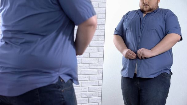 Plump man buttoning up tight shirt, oversize clothing problem, appearance - Foto, imagen
