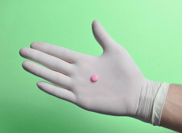 Comprimido rosa en mano médica con guantes de látex blanco sobre fondo azul. Médico cóncavo
 - Foto, imagen