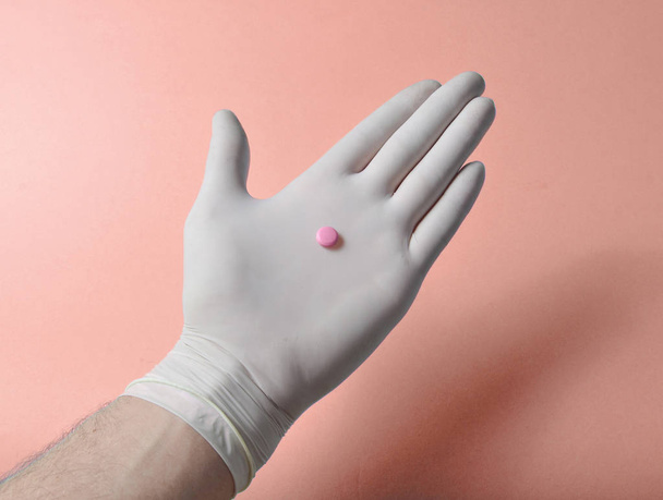 Comprimido rosa na mão médica com luvas de látex branco sobre um fundo azul. Conceito médico
 - Foto, Imagem