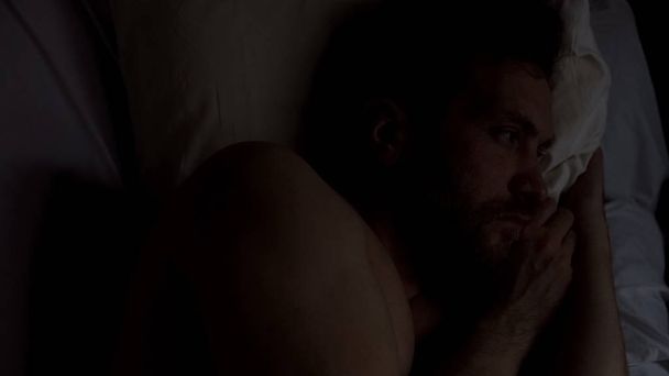 Upset young male suffering insomnia, lying alone in bed, thinking about problems - 写真・画像