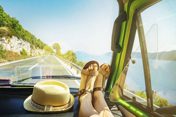 Viaje de verano con piernas femeninas jóvenes en el salpicadero dentro de la clásica furgoneta oldtimer que cruza junto a la costa del mar
 - Foto, imagen
