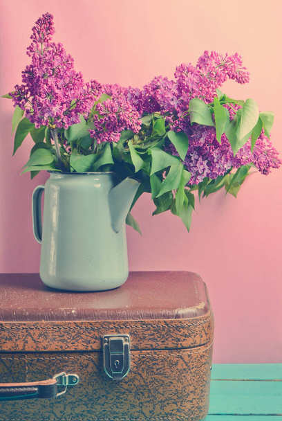 ヴィンテージ スーツケース ピンクの背景に古いホーロー ティーポットにライラックの花束。レトロなスタイルまだ lif - 写真・画像