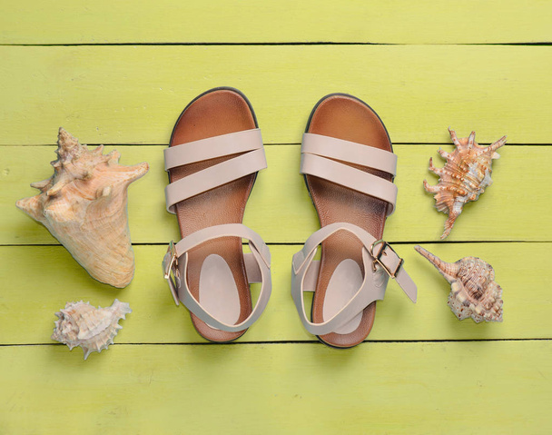 Sandálias femininas na moda, conchas no chão de madeira amarelo. O conceito de relaxar na praia. Vista superior
 - Foto, Imagem