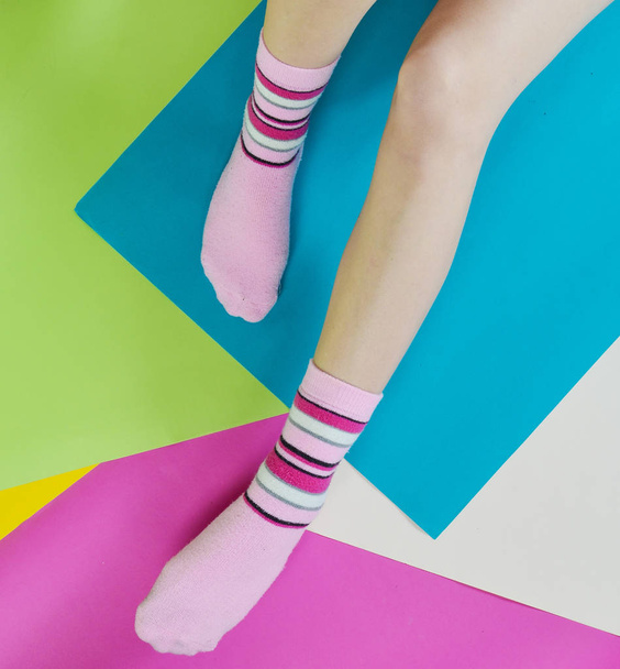 nackte weibliche Füße in Socken, die auf einem bunten Papierhintergrund posieren. Ansicht von oben - Foto, Bild