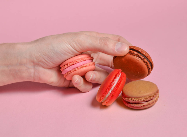 Colored macaroons in hand close-up on a pink backgroun - 写真・画像