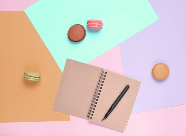 Colored macaroons cookies, diary with a pen on pastel background. Top view. Minimalis - Фото, зображення