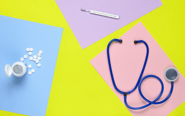 medizinisches Gerät auf farbigem Papierhintergrund. Stethoskop, Thermometer, Vitaminflasche. Medizinkonzept. Top-Konkurrenz - Foto, Bild