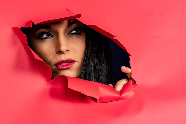 Nádherná brunetka model vkrádá na jasně růžovém papíru ukazující její tvář, nehty a rty - Fotografie, Obrázek