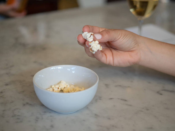 Woman manicured hand grabbing fresh popcorn out of a small bowl with wine - Foto, immagini