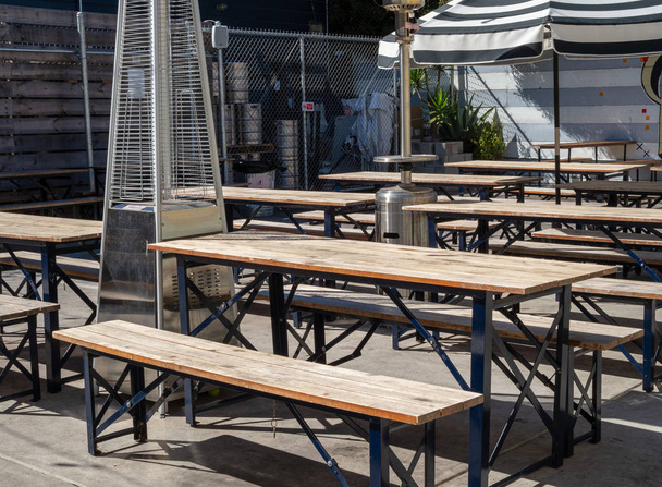 Outdoor picnic tables and umbrellas in an outdoor restaurant brewery dining area during sunny day - Photo, Image