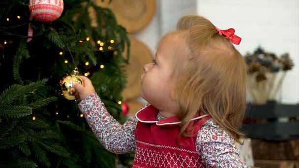 Μικρό κορίτσι διακόσμηση το χριστουγεννιάτικο δέντρο. Μικρό κορίτσι παίζει με το παιχνίδι στο χριστουγεννιάτικο δέντρο - Φωτογραφία, εικόνα