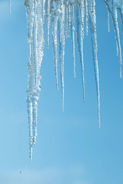 澄んだ空の背景につらら。氷が溶けると、屋根から落ちる人にとって危険であります。水滴。冬および早いばね. - 写真・画像