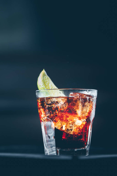Кубинский либр коктейль у барной стойки. Темный фон. Вертикаль
 - Фото, изображение