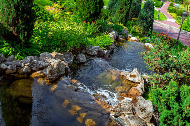 Cascada artificial tipo cascada con agua corriente hasta la acera peatonal con linternas para caminar y recreación
. - Foto, Imagen