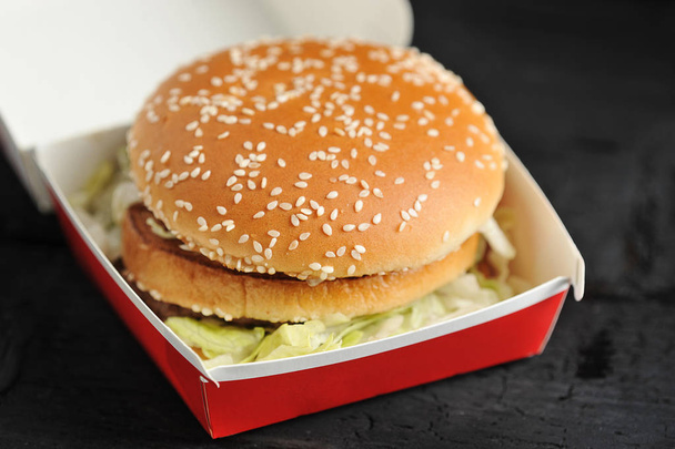Burger in a red box with a bun with sesame seeds close-up - Fotó, kép