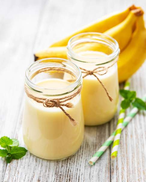 Bananen, yoghurt en verse bananen op een houten achtergrond - Foto, afbeelding