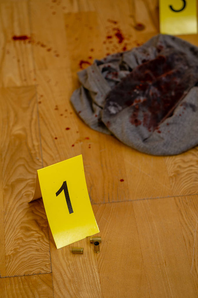 Bullet casings. bloody clothes, and gun next to markers at crime scene - Foto, imagen