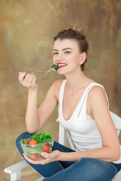 Giovane donna sana seduta sulla sedia bianca e mangiare insalata di verdure biologiche
. - Foto, immagini