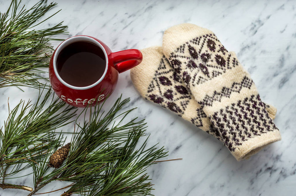 Knitted mittens, a red large cup of coffee and a pine branch. Concept winter. Close up - Foto, imagen