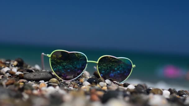 Zonnebril liggend op het zand. Weerspiegeld in een zonnebril golven, zee en hemel. - Video