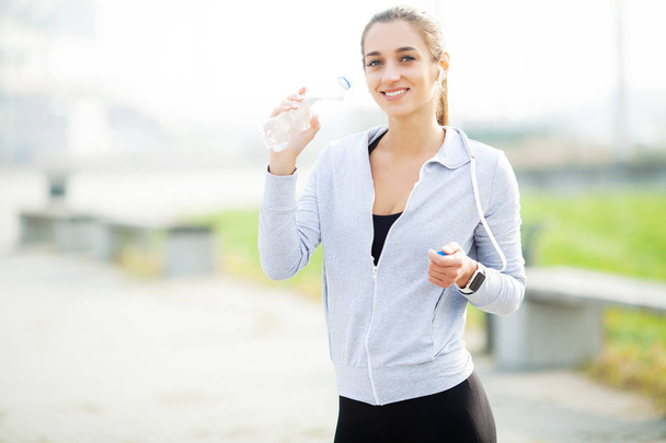 Спорт на открытом воздухе. Спортивная женщина в наушниках пьет воду
 - Фото, изображение