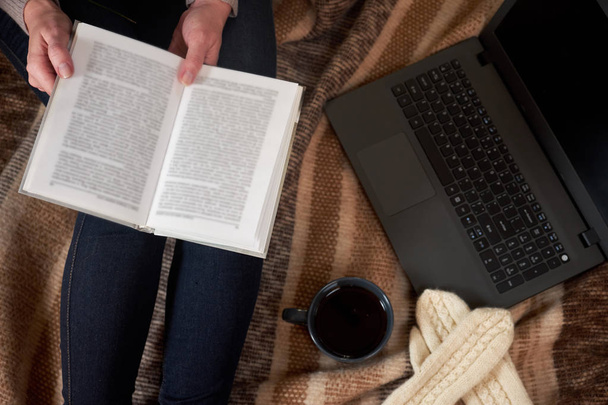 Woman with a Cup of tea, a book,  mittens and a laptop on a blanket. Selective focus - Фото, зображення