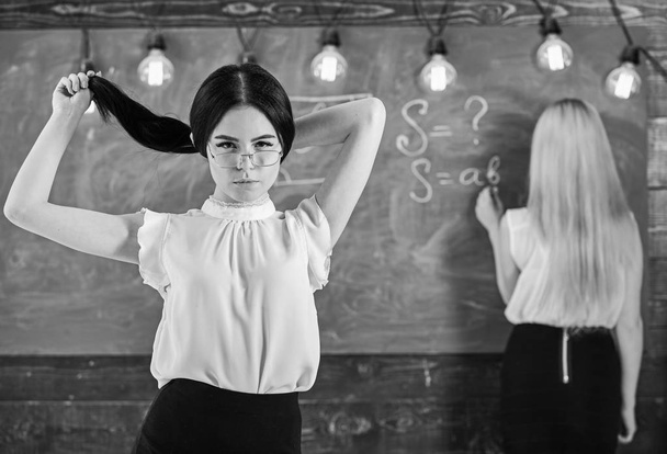 Students and trainees concept. Attractive women preparing for lesson. Student, teacher in eyeglasses stand in classroom. Girl looks attractive while lady writing on chalkboard background, defocused - Zdjęcie, obraz