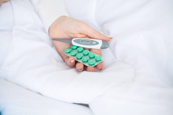 Cold and flu. Woman hold termometr and blister pills in hand, lying on the bed - Foto, imagen