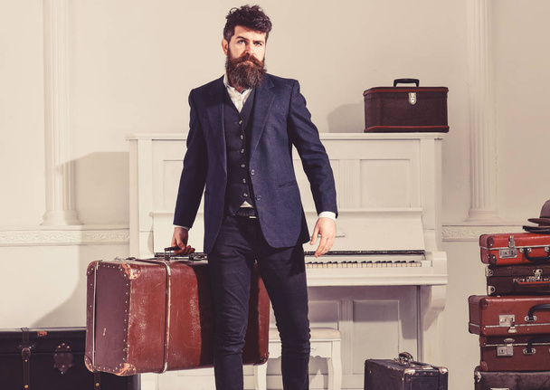 Man, traveller with beard and mustache with baggage, luxury white interior background. Baggage and travelling concept. Macho stylish on strict face stands and carries big vintage suitcase - Valokuva, kuva