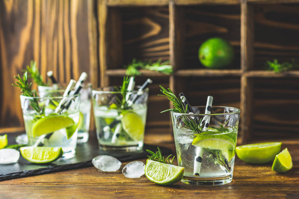 Cocktail frais avec citron vert, glace et romarin, cocktail de mojito dans un bourdonnement sur une table rustique, mise au point sélective, faible profondeur du champ
. - Photo, image