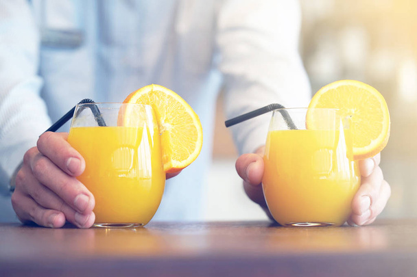 The barman gives two glasses of orange juice to the client of the hotel restaurant. The waiter transfers the order for two orange juice to the client of the hotel bar. The concept of service. Toning - Photo, Image
