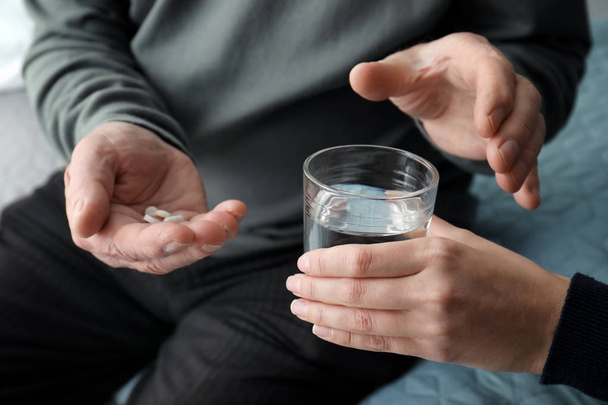 Young woman giving water to senior man with pills, closeup - Photo, image