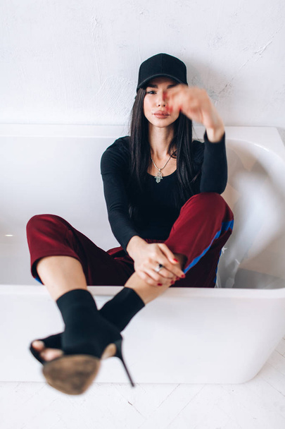 Portrait of a brunette girl in a cap and sportswear. Natural light. Red sweatpants, black top, black cap. - Valokuva, kuva