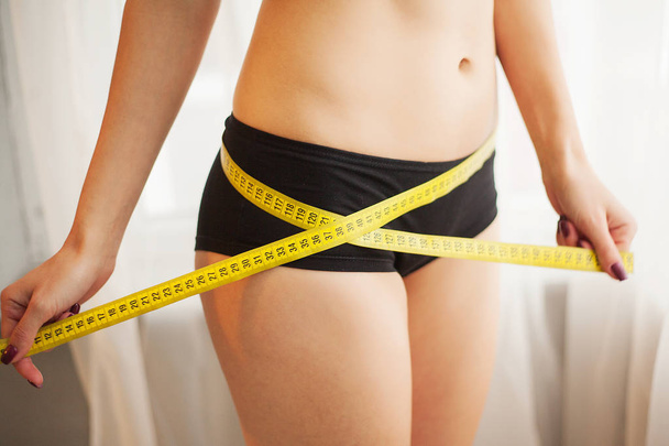 Hands measuring waist with a tape. Slim and healthy woman at her home - Foto, Bild