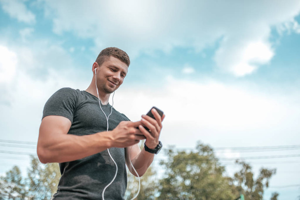 The athlete is holding a smartphone. Happy smiling, listening to music communicates on social networks. A man athlete calls ringing in headphones. - 写真・画像