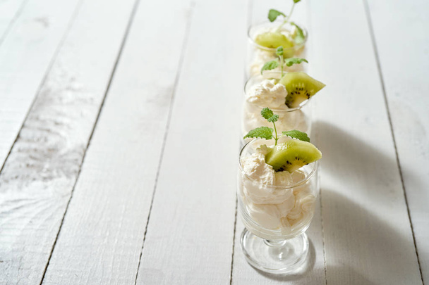 Склянка десерту зі збитими вершками зі свіжим листом м'яти та ківі на білому дерев'яному столі
. - Фото, зображення