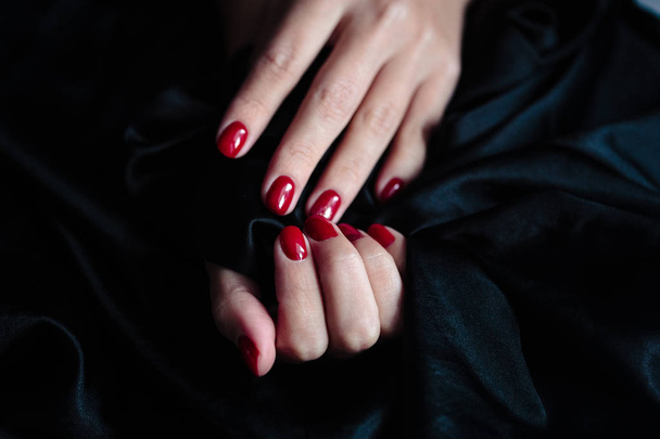 Gorgeous manicure, clssic red color nail polish, closeup photo. Female hands over dark fur background  - Valokuva, kuva