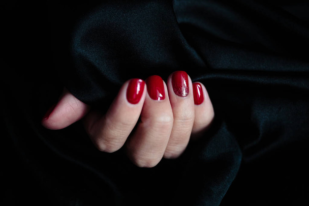 Gorgeous manicure, clssic red color nail polish, closeup photo. Female hands over dark fur background  - Foto, afbeelding
