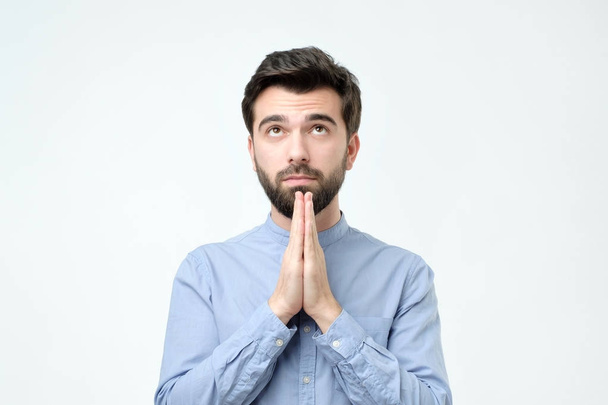 Guy in blue shirt holding hands in pray and gazing at camera hopefu - Foto, Imagem