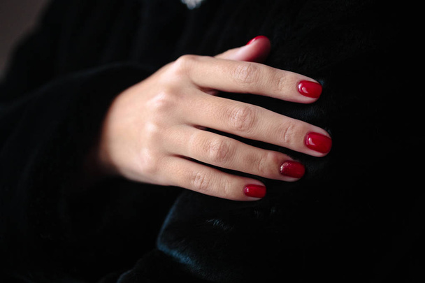 Gorgeous manicure, clssic red color nail polish, closeup photo. Female hands over dark fur background  - Foto, imagen